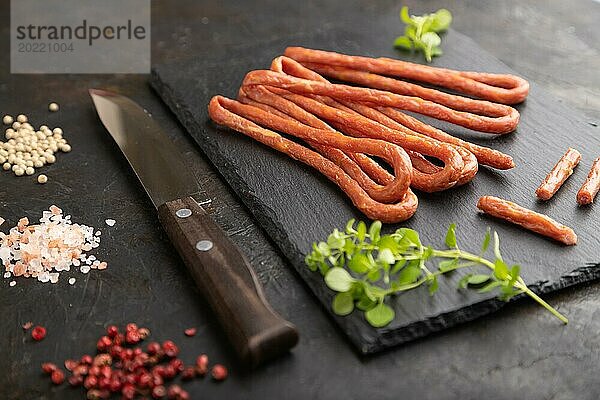 Traditionelle polnische geräucherte Schweinefleischwurst kabanos auf einem Schieferschneidebrett mit Salz und Pfeffer auf schwarzem Betonhintergrund. Seitenansicht  Nahaufnahme  selektiver Fokus