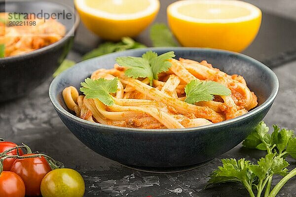 Grießnudeln mit Tomaten Pesto Soße  Orange und Kräutern in Schalen auf schwarzem Betonhintergrund. Seitenansicht  Nahaufnahme  selektiver Fokus