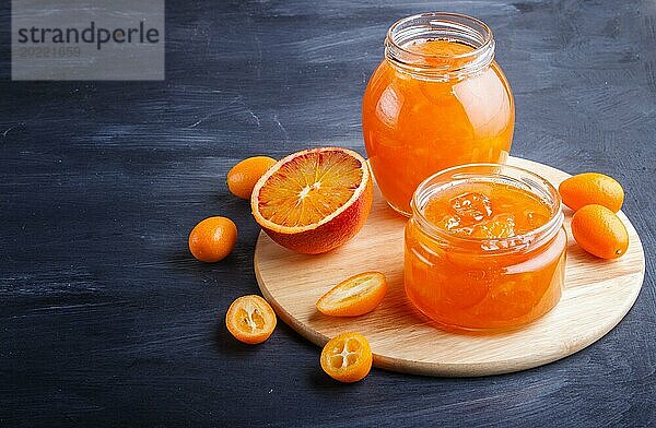 Orangen und Kumquatmarmelade in einem Glas mit frischen Früchten auf schwarzem Holzhintergrund. Hausgemacht  Nahaufnahme  Kopierraum