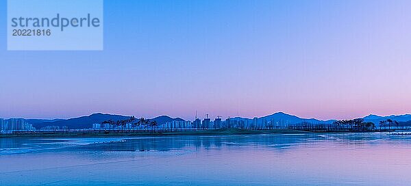 Pastellfarbener Himmel in der Dämmerung spiegelt sich über einem ruhigen See mit scherenschnittartiger Landschaft in Südkorea