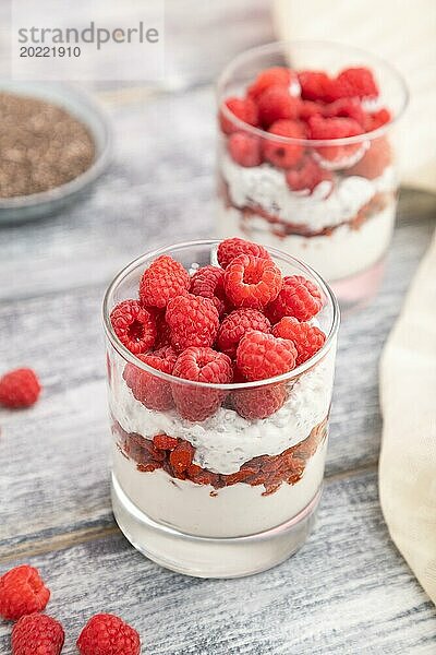 Joghurt mit Himbeeren  Goji Beeren und Chia Samen im Glas auf grauem Holzhintergrund und Leinenstoff. Seitenansicht  Nahaufnahme  selektiver Fokus