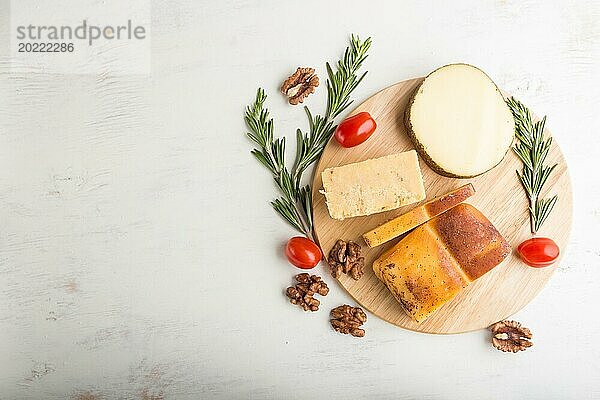 Geräucherter Käse und verschiedene Käsesorten mit Rosmarin und Tomaten auf einem Holzbrett auf einem weißen Holzhintergrund. Draufsicht  flat lay  copy space