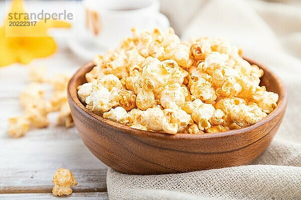 Popcorn mit Karamell in einer Holzschüssel und eine Tasse Kaffee auf einem weißen Holzhintergrund und Leinenstoff. Seitenansicht  Nahaufnahme  selektiver Fokus