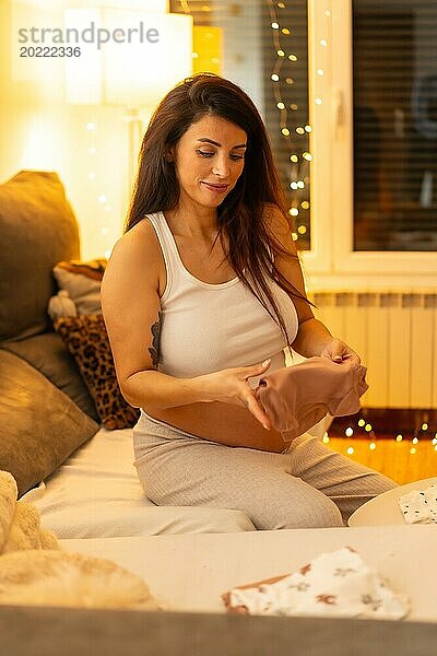 Vertikales Porträt einer ruhigen Szene einer schönen schwangeren Frau  die ihre Kleidung faltet und die Tasche für die Geburt des Kindes vorbereitet