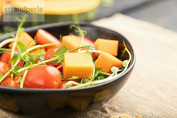 Vegetarischer Gemüsesalat aus Tomaten  Kürbis  mikrogrünen Erbsensprossen auf schwarzem Betonhintergrund und Leinentuch. Seitenansicht  Nahaufnahme  selektiver Fokus