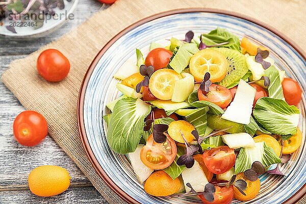 Vegetarischer Salat aus Pac Choi Kohl  Kiwi  Tomaten  Kumquat  Mikrogrünsprossen auf grauem Holzhintergrund und Leinentuch. Draufsicht  Nahaufnahme  selektiver Fokus
