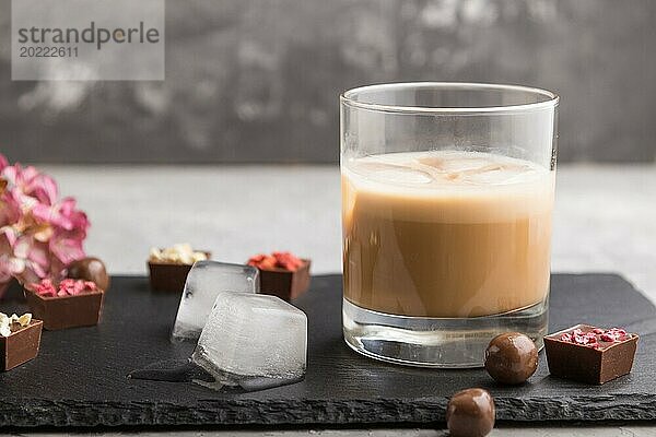 Süßer Schokoladenlikör mit Eis in einem Glas mit Schokoladenbonbons auf einem grauen Betonhintergrund und einer schwarzen Steinschiefertafel. Seitenansicht  Nahaufnahme  selektiver Fokus