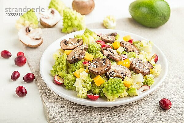 Vegetarischer Salat aus Romanesco Kohl  Champignons  Preiselbeeren  Avocado und Kürbis auf weißem Holzhintergrund und Leinentuch. Seitenansicht  Nahaufnahme  selektiver Fokus