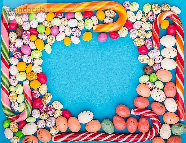Bunte Rahmen von bunten Süßigkeiten auf einem blauen Hintergrund. Weihnachtsstangen  Schokoladeneier  Karamell Dragees. Kreis Kopie Raum  Draufsicht  flach legen