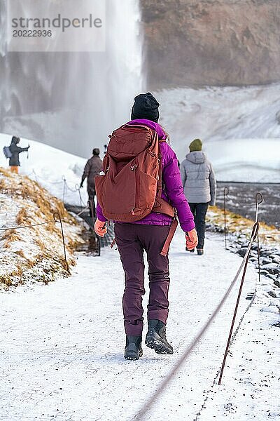 Eine Frau besucht Island im Winter mit einem Rucksack am Seljalandsfoss Wasserfall