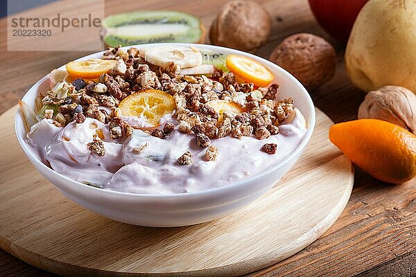 Vegetarischer Salat aus Bananen  Äpfeln  Birnen  Kumquats  Kiwi mit Granola und Joghurt auf braunem woodem Hintergrund  Nahaufnahme  selektiver Fokus