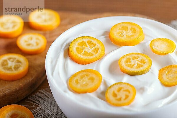 Griechischer Joghurt mit Kumquat Stücken in einem weißen Teller auf einem braunen Holzuntergrund  Nahaufnahme