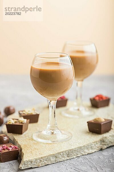 Süßer Schokoladenlikör im Glas mit Schokoladenbonbons auf einem grauen Betonhintergrund und einer Steinschiefertafel. Seitenansicht  Nahaufnahme  selektiver Fokus