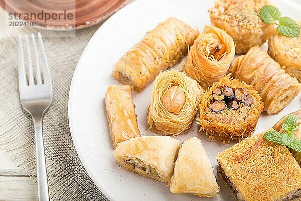 Traditionelle arabische Süßigkeiten (kunafa  baklava) und eine Tasse Kaffee auf einem weißen hölzernen Hintergrund und Leinenstoff. Seitenansicht  Nahaufnahme  selektiver Fokus