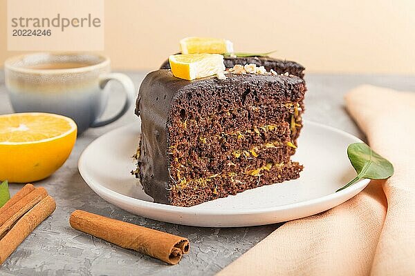 Hausgemachter Schokoladenkuchen mit Orange und Zimt mit einer Tasse Kaffee auf einem grauen Betonhintergrund mit orangefarbenem Textil. Seitenansicht  Nahaufnahme  selektiver Fokus