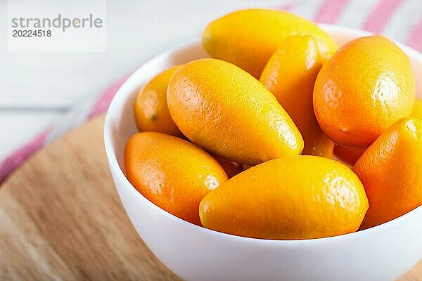 Kumquats in einem weißen Teller auf weißem Holzuntergrund  Nahaufnahme