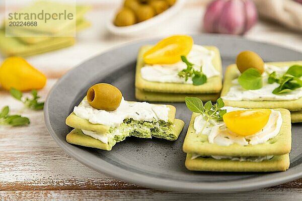 Grüne Cracker Sandwiches mit Frischkäse und Kirschtomaten auf weißem Holzhintergrund und Leinentextil. Seitenansicht  Nahaufnahme  selektiver Fokus