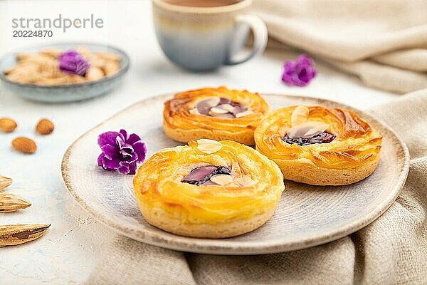 Kleine Käsekuchen mit Marmelade und Mandeln mit einer Tasse Kaffee auf weißem Betonhintergrund und Leinenstoff. Seitenansicht  Nahaufnahme  selektiver Fokus