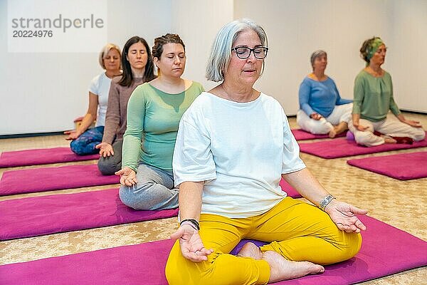 Gruppe reifer Frauen meditiert im Lotussitz auf Matten in einer Yogastunde