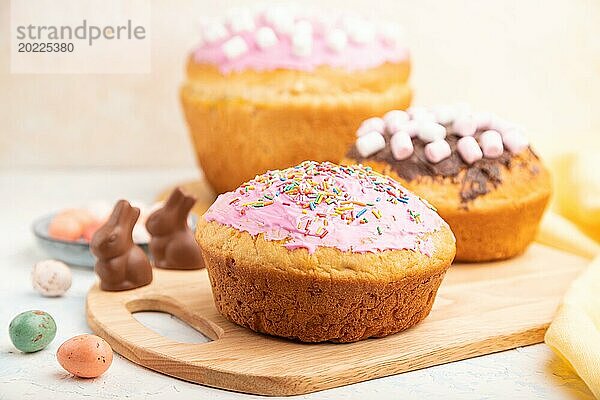 Hausgemachte glasierte und dekorierte Osterkuchen mit Schokoladeneiern und Kaninchen auf weißem Betonhintergrund und gelbem Textil. Seitenansicht  Nahaufnahme  selektiver Fokus