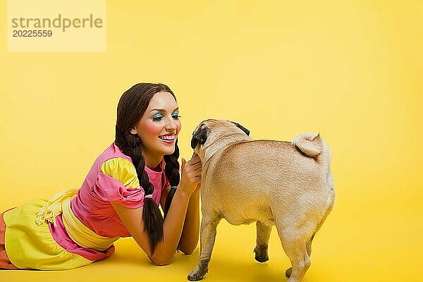 Glückliches Mädchen wie niedliche Puppe füttern einen kleinen Hund auf gelbem Hintergrund