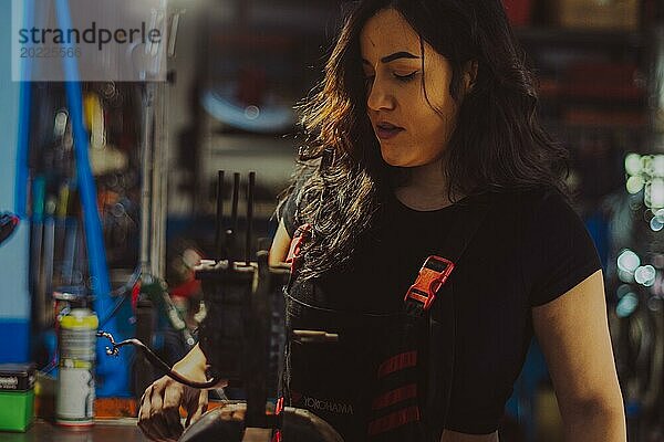 Fokussierte Mechanikerin  die ein Motorteil eines Rollers in einer Werkstatt repariert  eine komplette Werkzeugtafel im Hintergrund mit Bokeh Effekt  traditionelle männliche Berufe von Mixed race Latino Frau