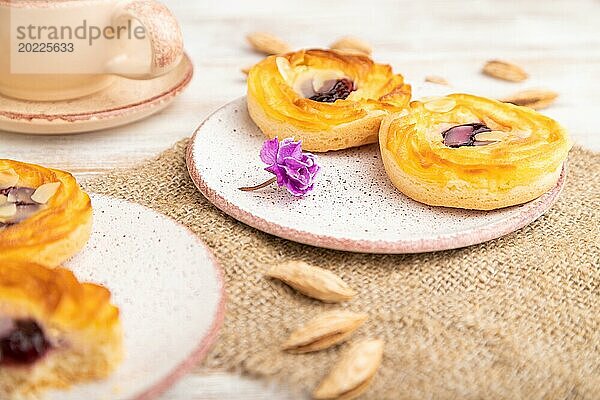 Kleine Käsekuchen mit Marmelade und Mandeln mit einer Tasse Kaffee auf einem weißen Holzhintergrund und Leinenstoff. Seitenansicht  Nahaufnahme  selektiver Fokus