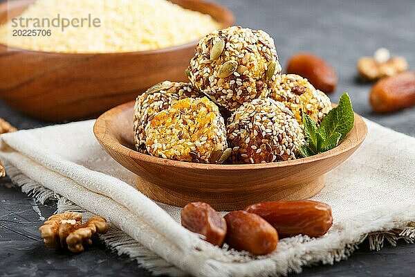 Energiekugelkuchen mit getrockneten Aprikosen  Sesam  Cornflakes  Leinen  Walnüssen und Datteln mit grünen Minzblättern in einer Holzschale auf schwarzem Betonhintergrund. Leinenserviette  Seitenansicht  Nahaufnahme  selektiver Fokus  vegane hausgemachte Süßigkeiten