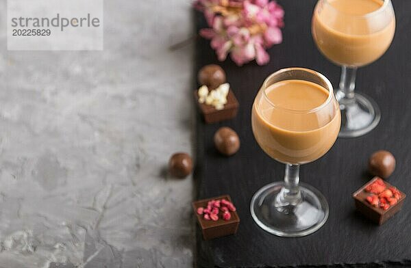 Süßer Schokoladenlikör im Glas mit Schokoladenbonbons auf einem grauen Betonhintergrund und einer schwarzen Schiefertafel. Seitenansicht  Kopierraum  selektiver Fokus