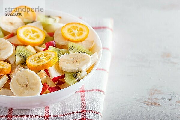 Vegetarischer Salat aus Bananen  Äpfeln  Birnen  Kumquats und Kiwi auf Leinentischdecke  Nahaufnahme  selektiver Fokus  Copy Space. weißer Holzhintergrund