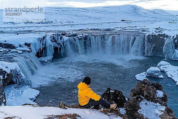 Abenteuerlustige Frau im Winter in Island mit Blick auf den gefrorenen Godafoss Wasserfall