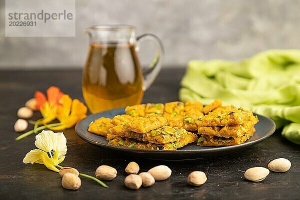 Traditionelles iranisches Dessert Sohan mit einem Glas grünem Tee auf einem schwarzen Betonhintergrund und grünem Textil. Seitenansicht  Nahaufnahme  selektiver Fokus