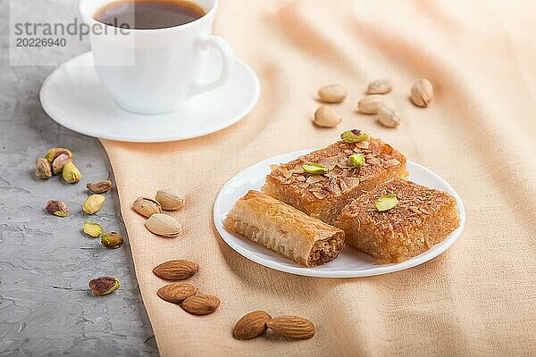 Traditionelle arabische Süßigkeiten (basbus  kunafa  baklava) und eine Tasse Kaffee auf einem grauen Betonhintergrund und orangefarbenem Textil