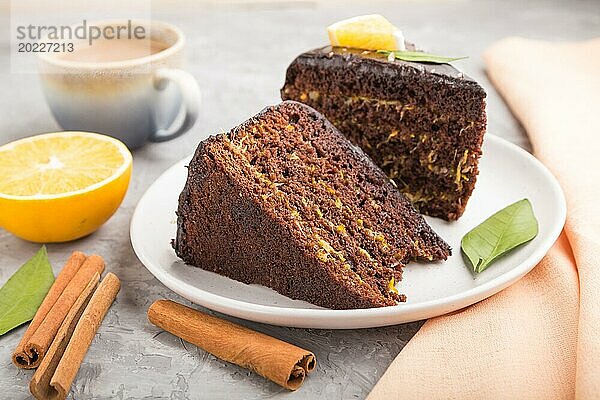 Hausgemachter Schokoladenkuchen mit Orange und Zimt mit einer Tasse Kaffee auf einem grauen Betonhintergrund mit orangefarbenem Textil. Seitenansicht  Nahaufnahme  selektiver Fokus