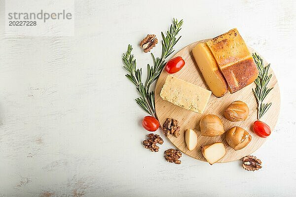 Geräucherter Käse und verschiedene Käsesorten mit Rosmarin und Tomaten auf einem Holzbrett auf einem weißen Holzhintergrund. Draufsicht  flat lay  copy space