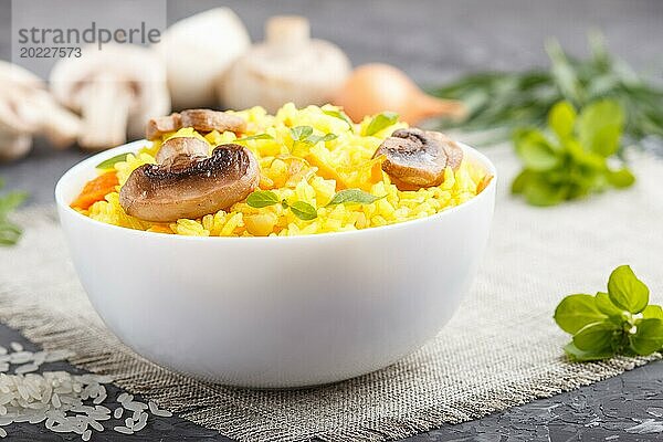 Gelber gebratener Reis mit Champignons  Kurkuma und Oregano in weißer Keramikschale auf schwarzem Betonhintergrund. Seitenansicht  Nahaufnahme  selektiver Fokus