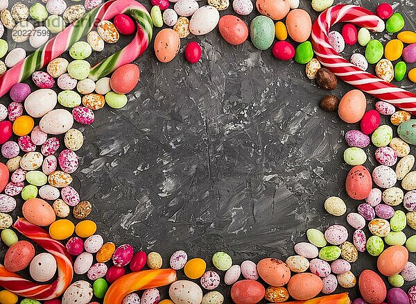 Bunte Rahmen von bunten Süßigkeiten auf einem schwarzen Beton Hintergrund. Weihnachtsstangen  Schokoladeneier  Karamell Dragees. Kreis Kopie Raum  Draufsicht  flach legen