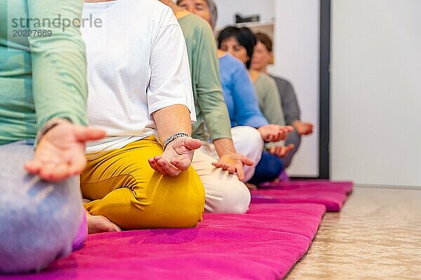 Ausgeschnittenes Foto mit Kopierraum und Fokus auf die Hände von Menschen  die auf einer Matte sitzend in einer Reihe meditieren