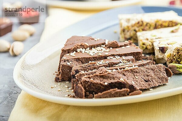 Traditionelle arabische Süßigkeiten Sesam Halva mit Schokolade und Pistazien und eine Tasse Kaffee auf einem grauen Hintergrund aus Beton und gelbem Textil. Seitenansicht  Nahaufnahme  selektiver Fokus