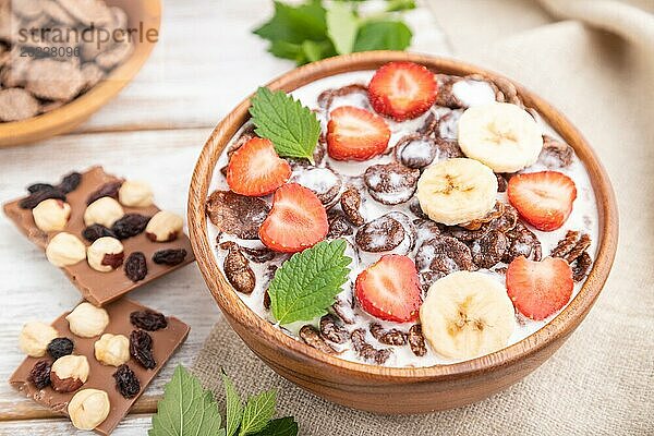 Schokoladen Cornflakes mit Milch und Erdbeeren in einer Holzschale auf weißem Holzhintergrund und Leinenstoff. Seitenansicht  Nahaufnahme  selektiver Fokus