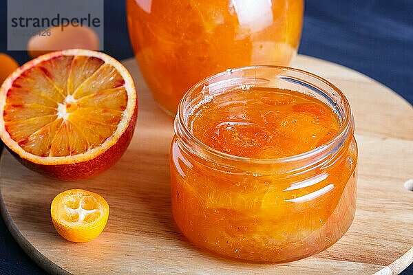 Orangen und Kumquatmarmelade in einem Glas mit frischen Früchten auf einem Küchenbrett aus Holz. Hausgemacht  Nahaufnahme