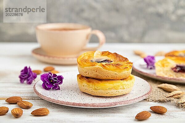 Kleine Käsekuchen mit Marmelade und Mandeln mit einer Tasse Kaffee auf einem weißen Holzhintergrund und Leinenstoff. Seitenansicht  Nahaufnahme  selektiver Fokus