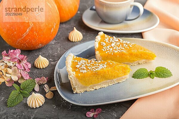 Zwei Stücke traditioneller amerikanischer Kürbiskuchen mit einer Tasse Kaffee auf einem schwarzen Betonhintergrund und orangefarbenem Textil. Seitenansicht  Nahaufnahme  Kontrast  selektiver Fokus