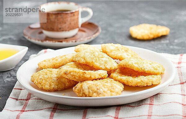 Traditionelle japanische Reis Chips Kekse mit Honig und Sojasauce auf einem weißen Keramikteller und eine Tasse Kaffee auf einem schwarzen Beton Hintergrund. Seitenansicht  Nahaufnahme  selektiver Fokus