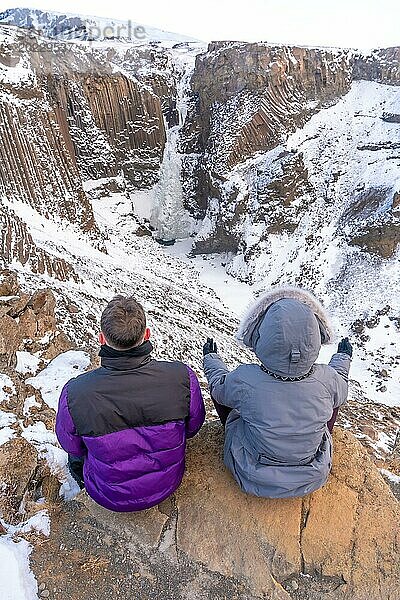 Ein Paar meditiert im Winter in Island am gefrorenen Wasserfall Hengifoss