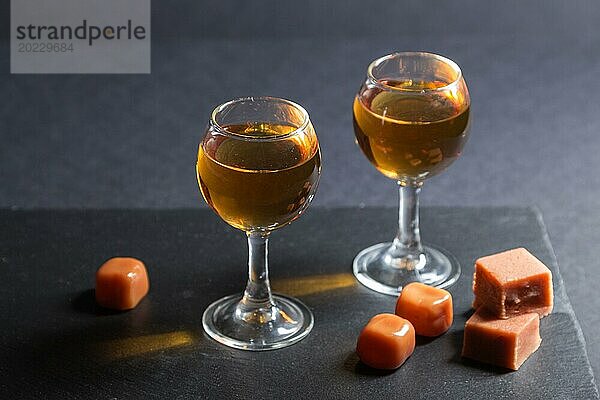 Glas Whiskey mit Karamellbonbons auf einem schwarzen Stein Schieferplatte auf schwarzem Hintergrund. Seitenansicht  Nahaufnahme  selektiver Fokus