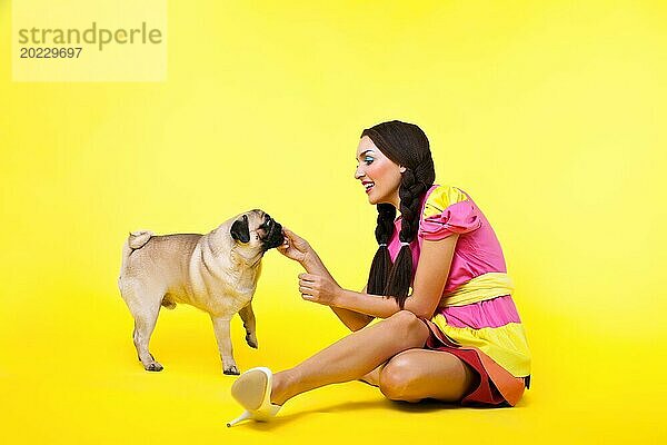 Nettes Mädchen in Puppenkleid füttern einen Hund mit Käse auf gelbem Hintergrund
