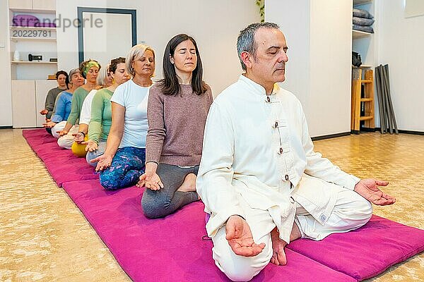 Yogalehrer leitet eine Meditation in einer Gemeinschaft auf einer Matte sitzend im Lotussitz