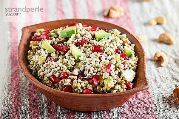 Salat aus gekeimtem Buchweizen  Avocado  Walnuss und Granatapfelkernen in einem Tonteller auf weißem Holzuntergrund. Seitenansicht  Nahaufnahme  selektiver Fokus