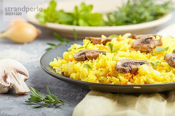 Gelber gebratener Reis mit Champignons  Kurkuma und Oregano auf blauem Keramikteller auf grauem Betonhintergrund und gelbem Textil. Seitenansicht  Nahaufnahme  selektiver Fokus